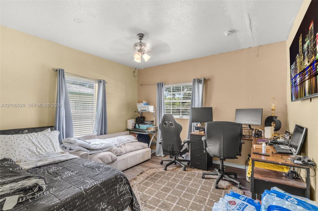 Room featuring dual-aspect windows, wood-finish flooring, and a central ceiling fan with integrated lighting