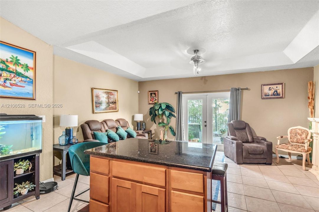 Tray ceiling with recessed lighting, center island with dark stone countertop and wood cabinetry, and double glass doors