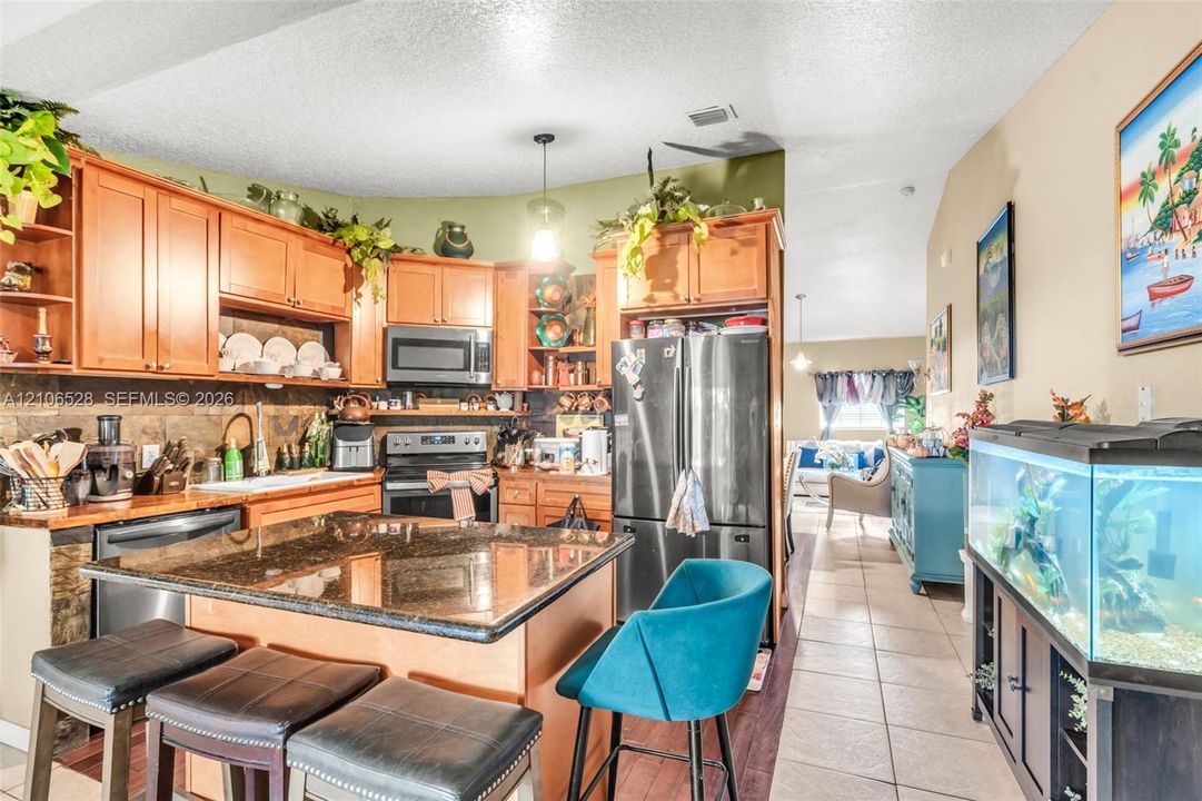 Kitchen featuring wood cabinetry, a stone-surfaced island, a tiled backsplash, and stainless steel appliances