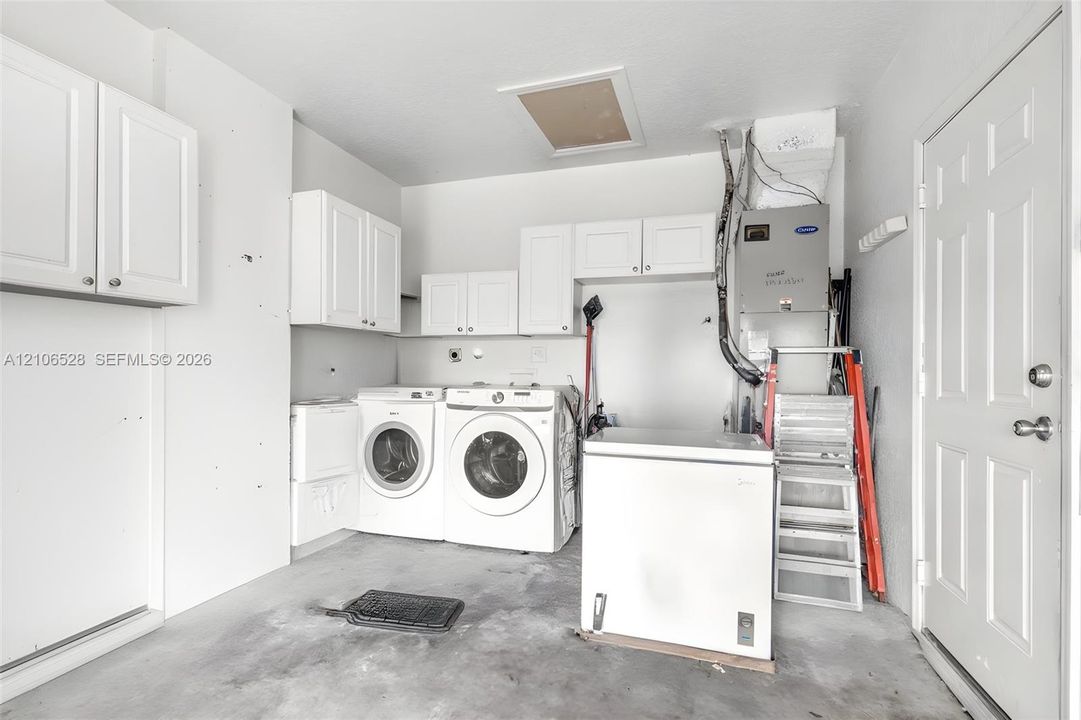 Utility area featuring wall-mounted white cabinetry, an HVAC system, and a six-panel entry door