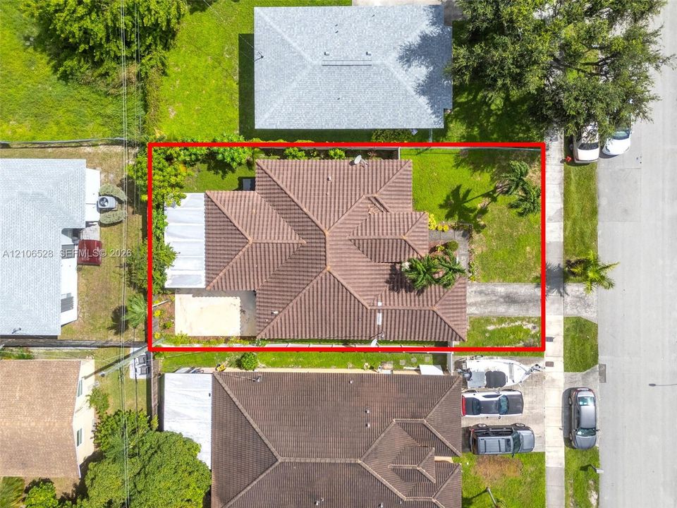 Aerial perspective of a property featuring a tile roof, paved driveway, concrete patio, and fenced grounds with mature landscaping