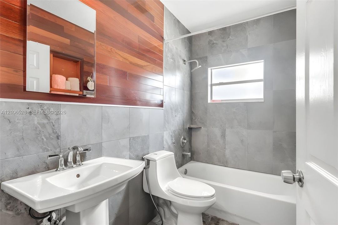 Bathroom featuring gray tile wall surround, horizontal wood-plank accent wall, white pedestal sink with chrome faucet, and integrated shower and tub combination