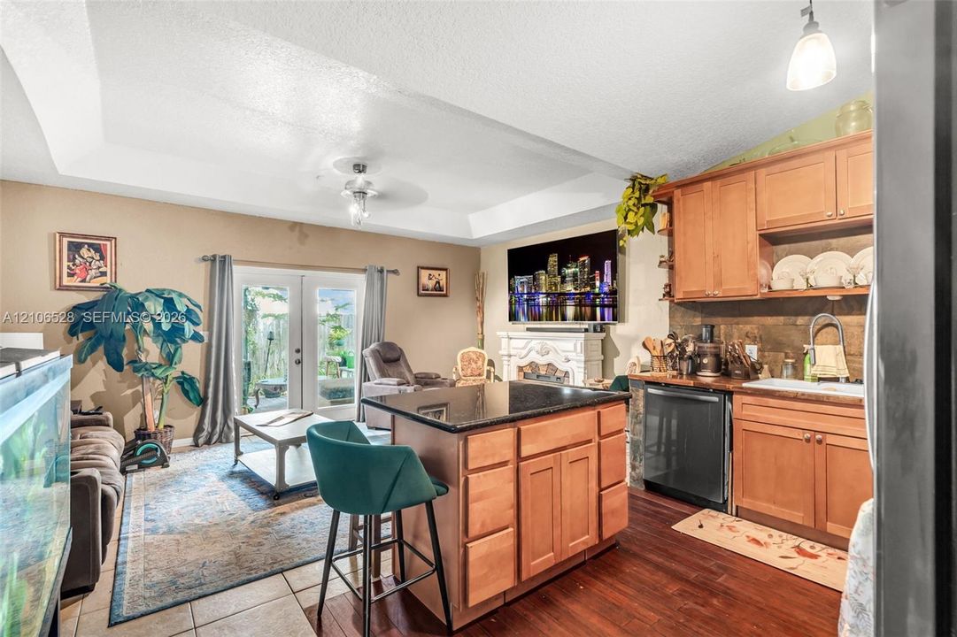 Kitchen featuring wood cabinetry, dark stone-topped island, tile backsplash, tray ceiling, and dual glass pane doors