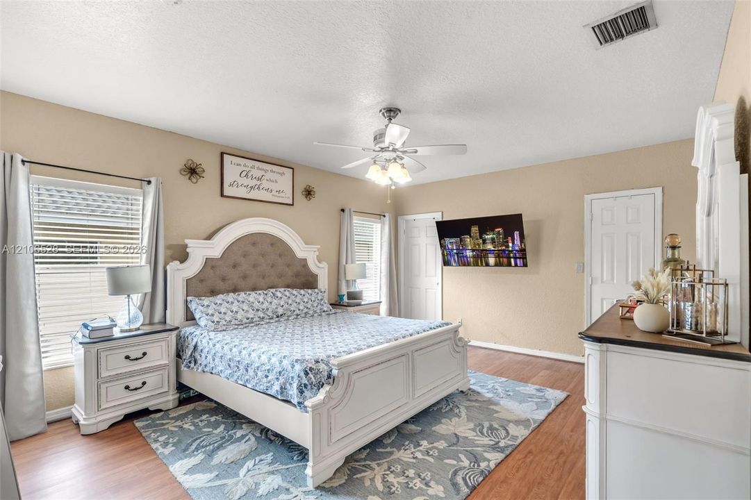 Spacious interior featuring wood-finish flooring, a ceiling fan with integrated lighting, dual windows with blinds, and paneled doors