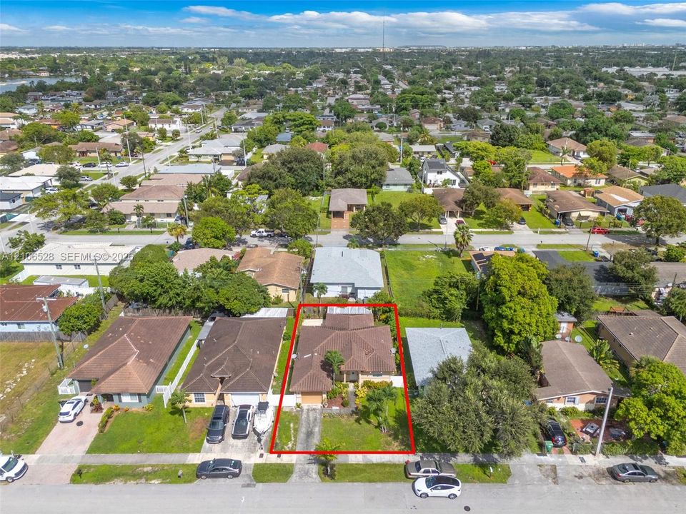 Aerial perspective of a residential property featuring a pitched shingle roof, paved driveway, integrated garage, and mature landscaping