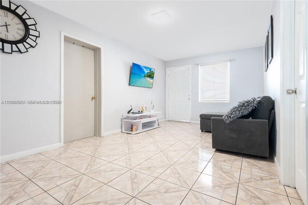 Neutral-toned interior space featuring patterned tile flooring, a recessed doorway, and a single-pane window with a horizontal blind