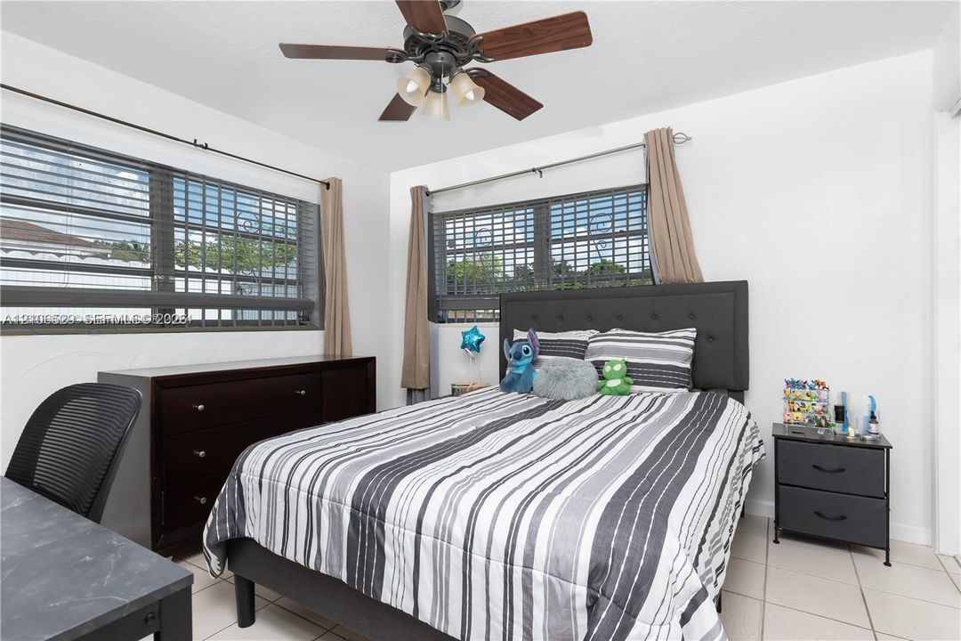 Bedroom featuring ceramic tile flooring, dual windows with integrated security bars, and a ceiling fan with multi-light fixture