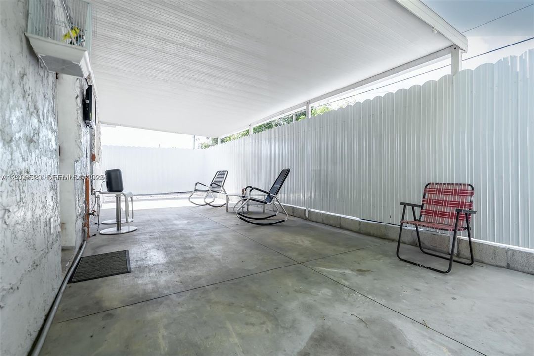 Covered patio featuring concrete flooring, a solid roof canopy, and white corrugated metal perimeter fencing