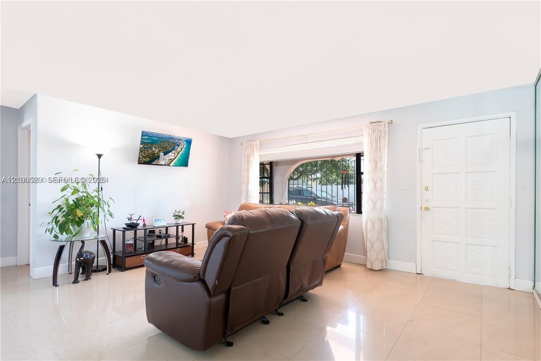 Living area featuring neutral tile flooring, a large picture window, and a panelled entry door