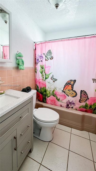 Bathroom featuring a grey vanity with a light-toned stone countertop, square-format wall tiling, a soaking tub with an integrated surround, and ceramic tile flooring
