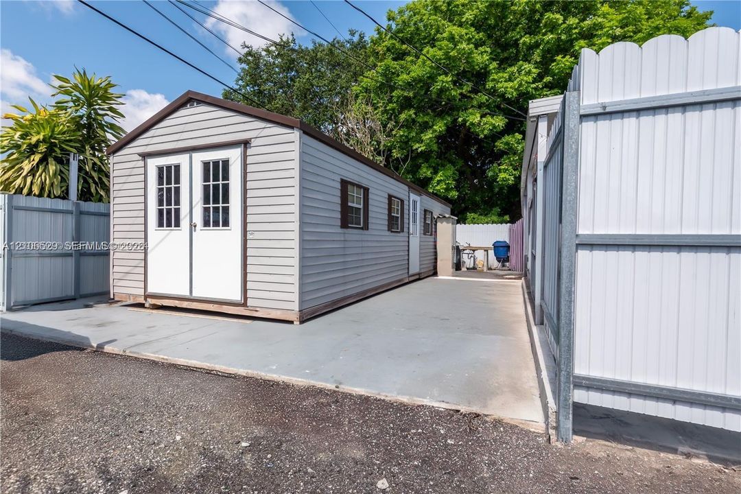 Outbuilding featuring horizontal vinyl siding, dual-entry doors, multiple windows, and a paved concrete pad