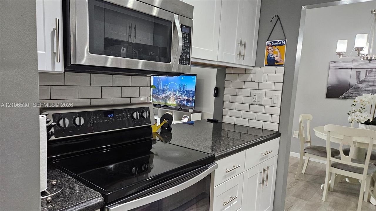 Kitchen featuring white shaker-style cabinetry, dark stone-finish countertops, stainless steel appliances, and a white subway tile backsplash