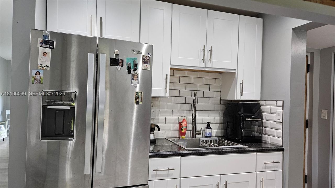 Kitchen area featuring white shaker-style cabinetry, dark countertops, a subway tile backsplash, and a stainless steel side-by-side refrigerator