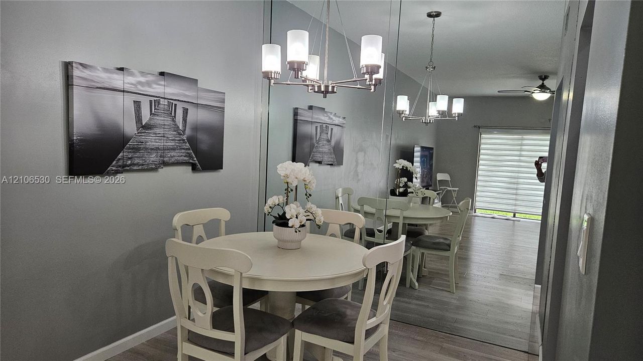 Dining area featuring wood-finish flooring, a full-length wall mirror, a multi-arm chandelier with frosted glass shades, and sliding glass doors