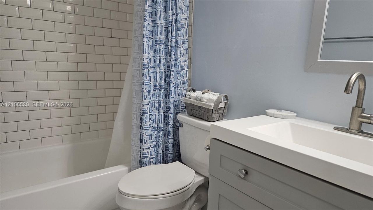 Bathroom featuring a white subway tile shower surround, grey vanity cabinet, white composite countertop with integrated sink, and a brushed nickel finish faucet