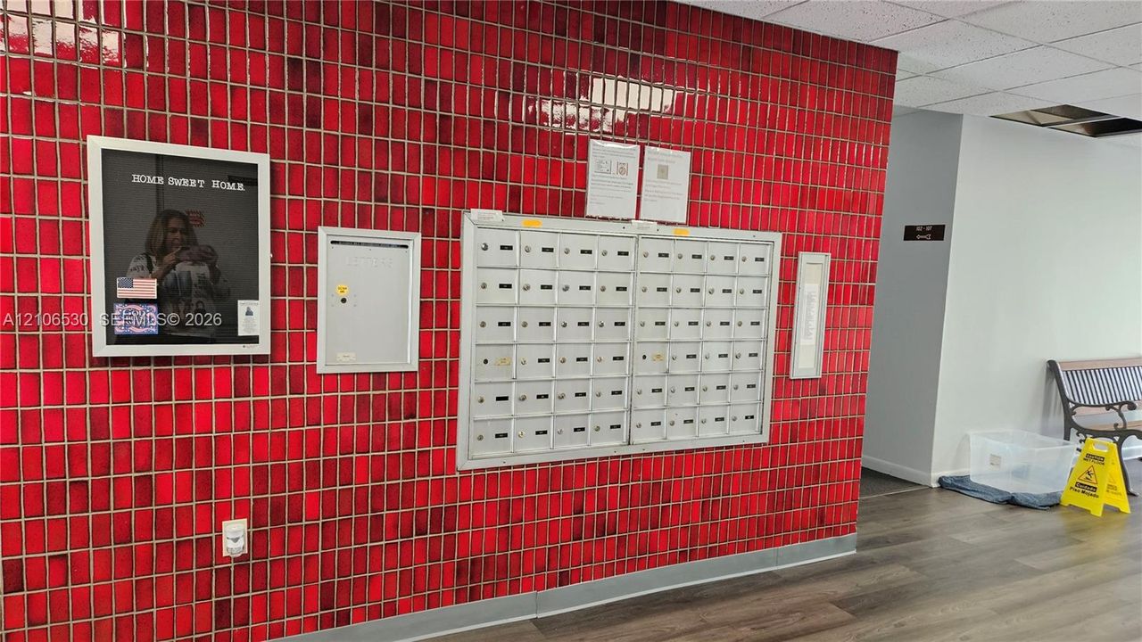 Glossy red square-tile feature wall with integrated metal mailboxes, secure recessed parcel locker, and wood-finish flooring