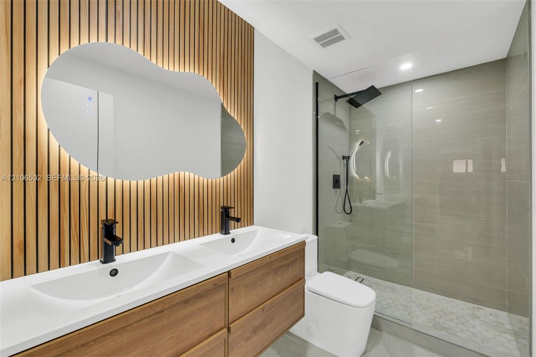 Double vanity featuring wood-finish cabinetry, matte black hardware, integrated lighting, and a vertical wood slat accent wall