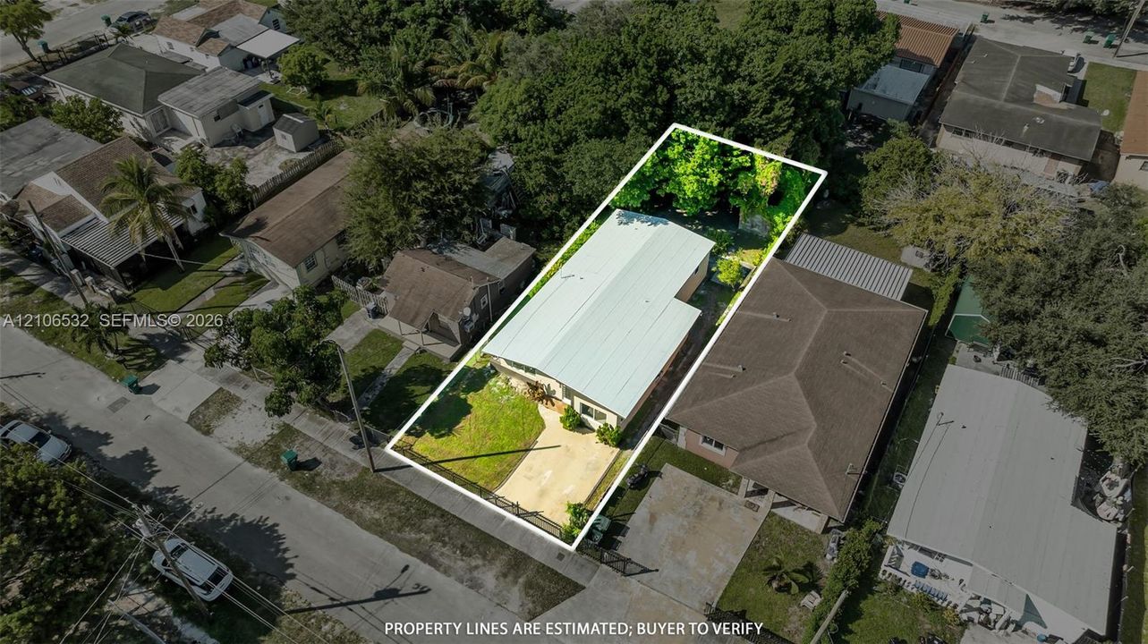 Aerial perspective of property featuring a metal roof, concrete driveway, front lawn, and mature trees in the rear grounds