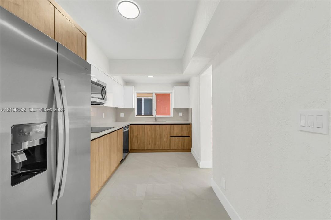 Kitchen featuring flat-panel wood cabinetry, white upper cabinets, stainless steel appliances, neutral stone-finish tile flooring, and light countertops