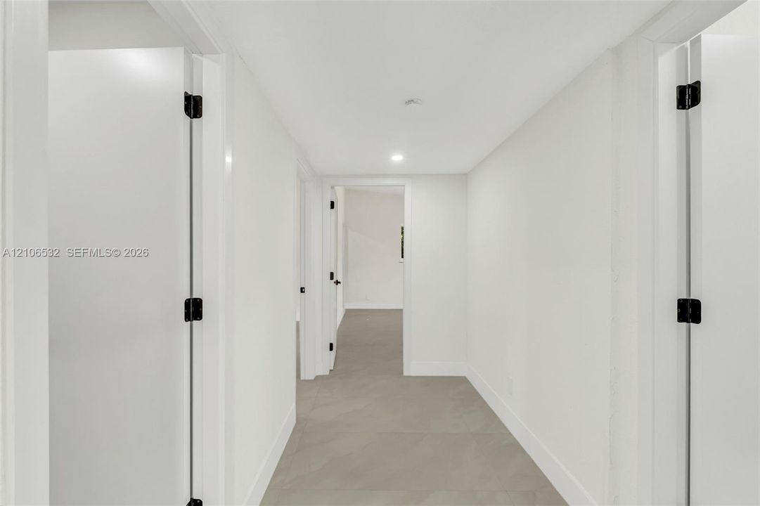 Hallway featuring large-format tile flooring, crisp white walls, recessed ceiling lighting, and solid-core doors with matte black hardware
