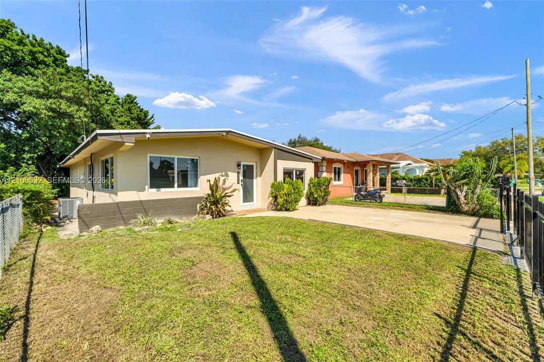 Single-story exterior featuring tan stucco siding, a concrete driveway, a front lawn, and metal perimeter fencing