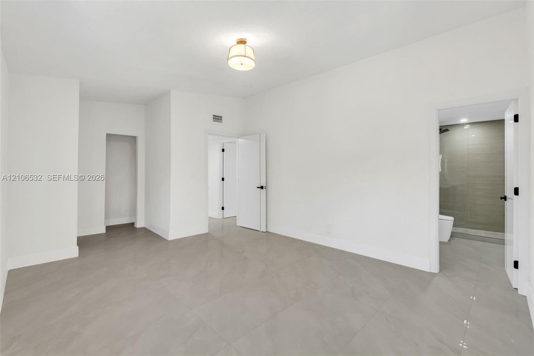 Neutral-toned large-format tile flooring, contemporary drum-style ceiling light fixture, and solid-core interior doors with matte black hardware