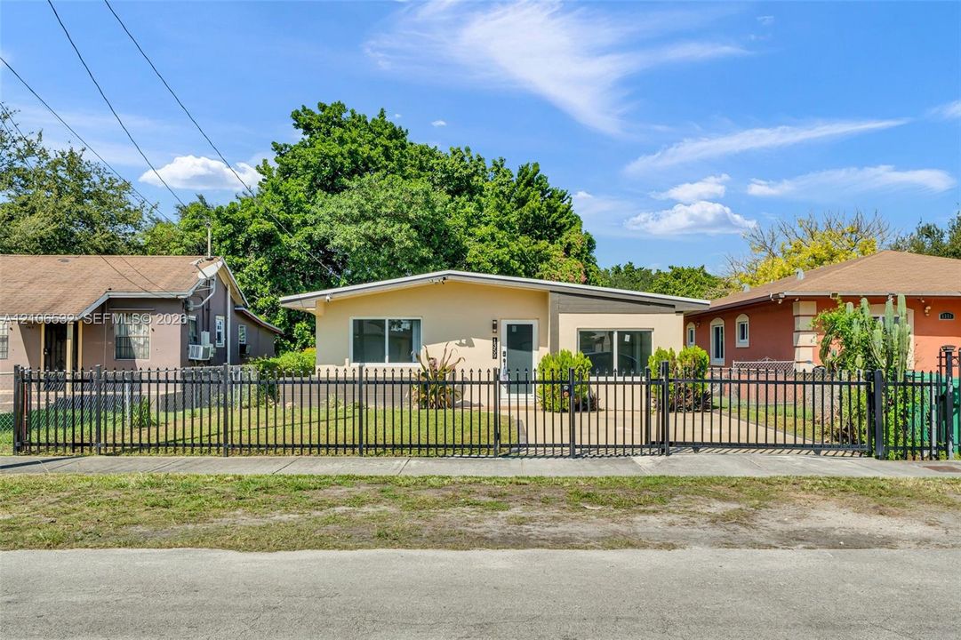 Exterior featuring a light-toned stucco façade, low-pitch roofline, dual-tone accent wall, and a full-perimeter metal fence