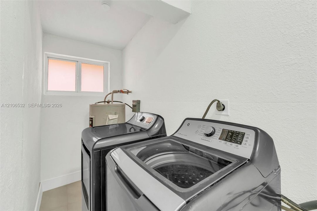 Utility room featuring neutral wall finishes, a sliding window, and a dedicated water heater