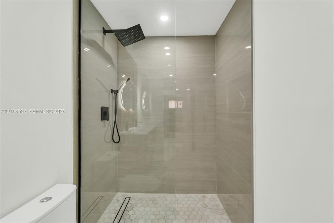 Walk-in shower featuring floor-to-ceiling tile, frameless glass enclosure, rainfall showerhead, handheld sprayer, and hexagonal tile flooring