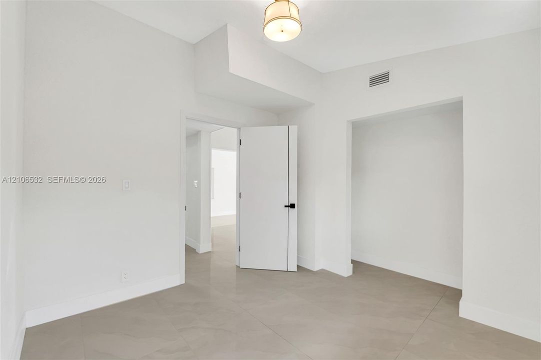 Interior space featuring large-format ceramic tile flooring, a semi-flush mount drum light fixture, and a solid-core door with matte black hardware