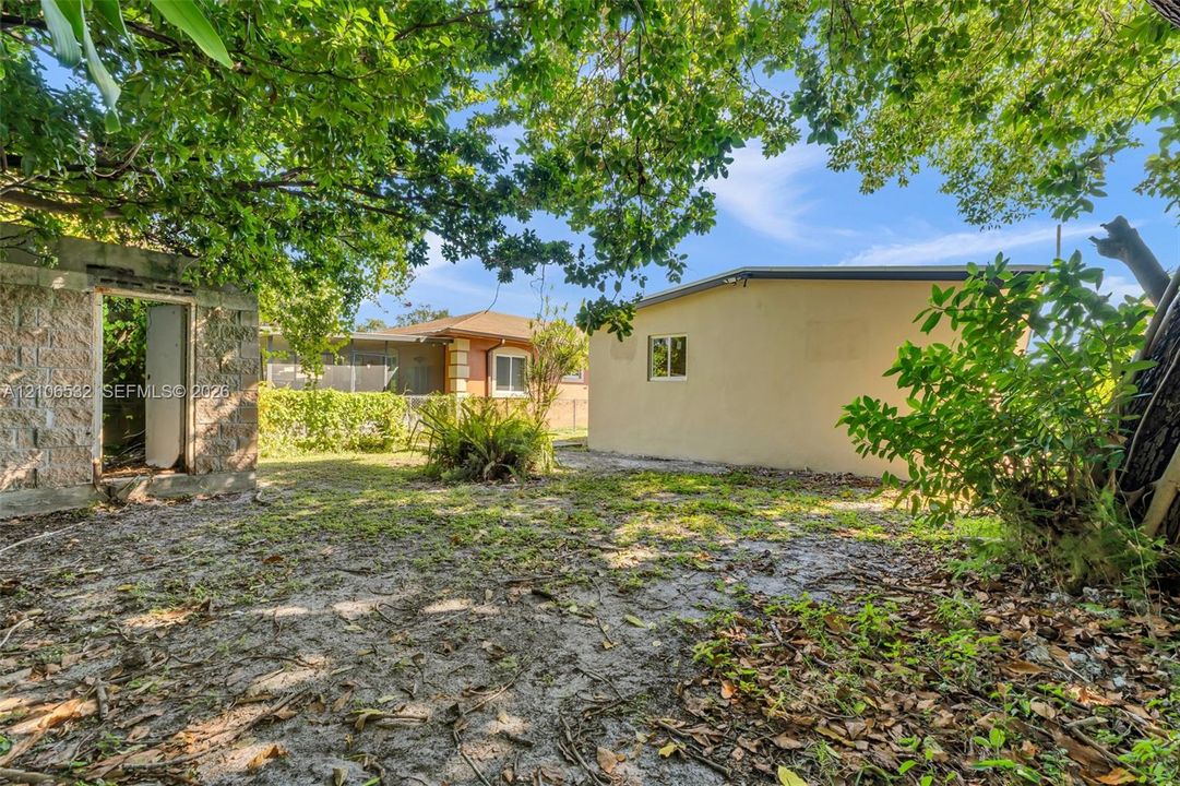 Backyard area featuring mature trees, a detached structure with stucco exterior, and a secondary masonry-walled enclosure