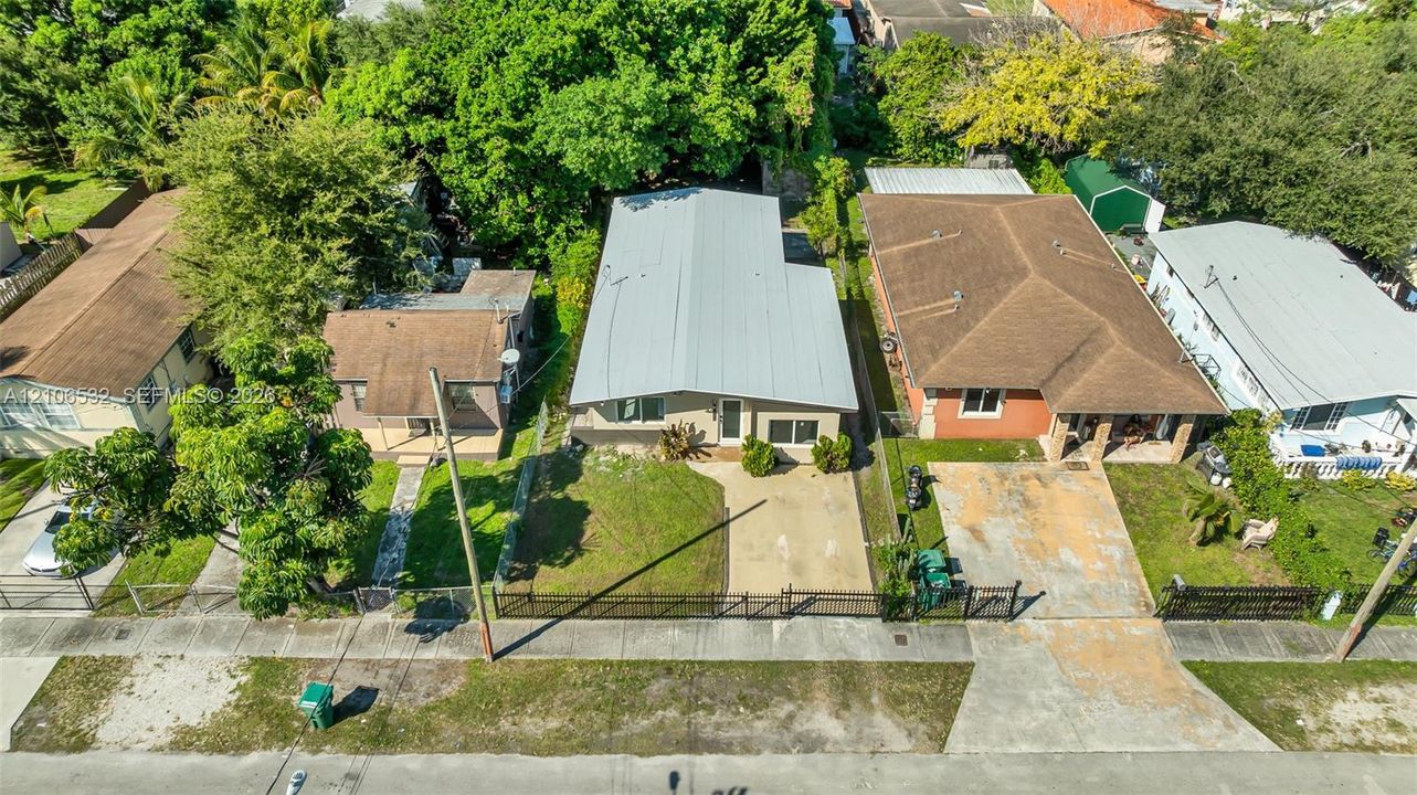 Aerial view of property featuring a metal roof, concrete driveway, and gated perimeter fencing