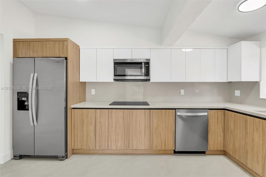 Kitchen featuring wood-finish lower cabinetry, white flat-panel upper cabinets, stainless steel appliances, and solid surface countertops