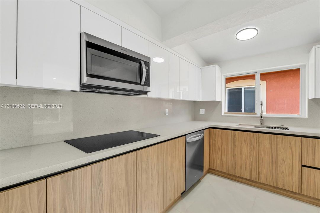 Kitchen featuring gloss-finish upper cabinetry, wood-finish lower cabinetry, stone-composite countertops, stainless steel appliances, and a single-basin undermount sink