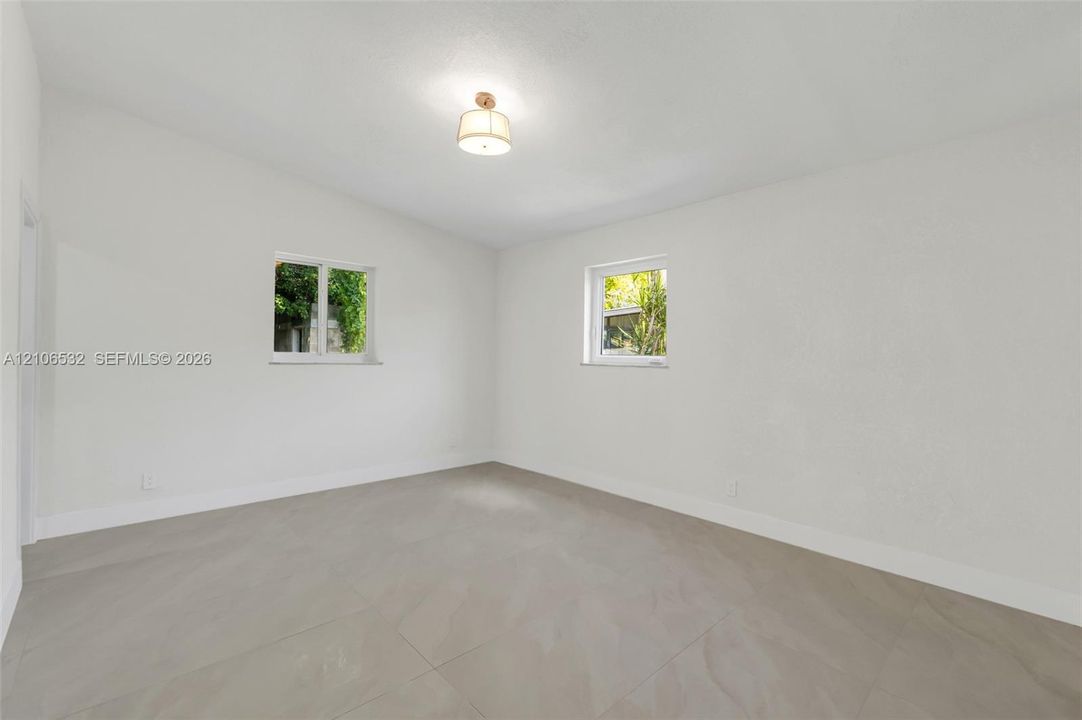 Interior room featuring neutral wall finishes, large-format tile flooring, dual windows, and a central ceiling-mounted light fixture