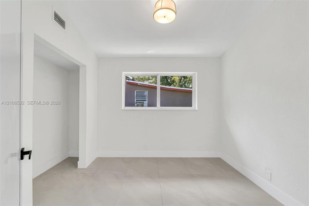 Neutral-toned tile flooring, recessed ceiling lighting, and a window providing natural illumination, finished with crisp white walls and an open-concept architectural cutout