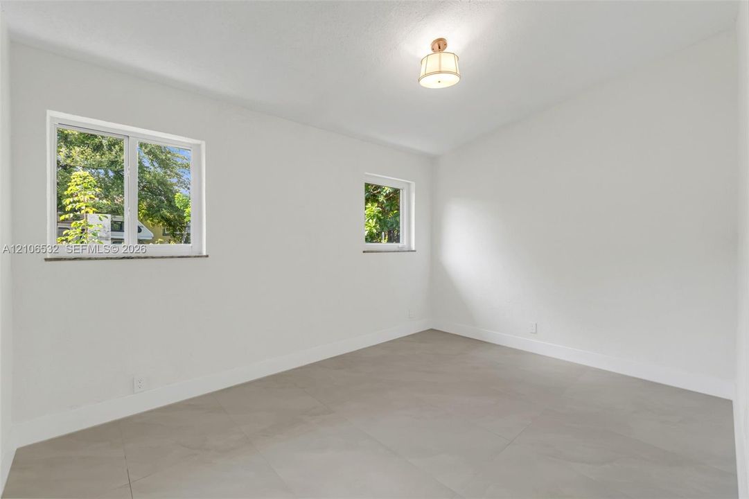 Neutral interior space featuring large-format ceramic tile flooring, two windows with stone sills, and a drum-style ceiling light fixture