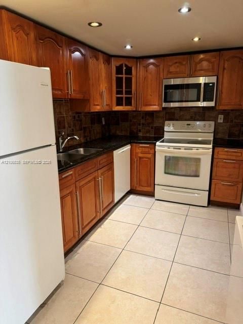 Kitchen featuring wood cabinetry with glass-front display panels, dark stone-style countertops, tiled backsplash, large-format floor tile, and recessed lighting