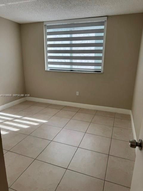 Neutral-toned interior room featuring large-format ceramic tile flooring, a textured ceiling, and a window equipped with striped horizontal roller shades