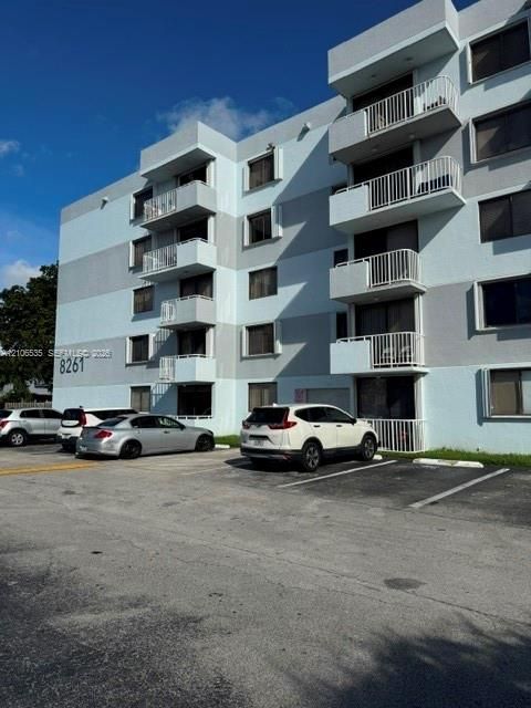 Multi-story exterior featuring a two-tone concrete facade, stacked private balconies with metal railings, and surface-level parking