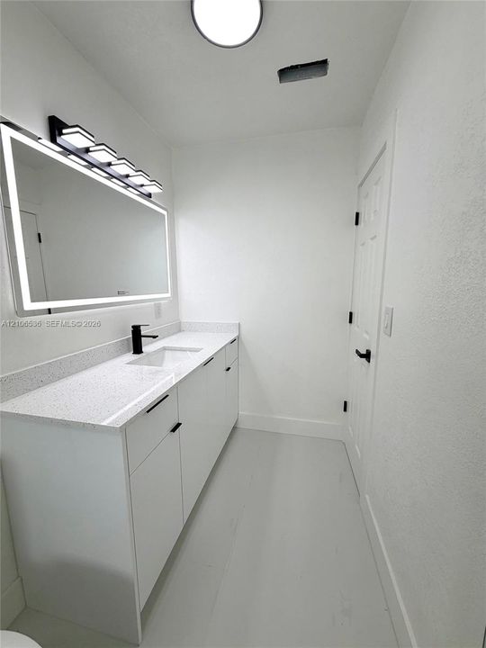 Modern vanity with a speckled countertop, integrated rectangular sink, matte black faucet, and a large backlit mirror with an integrated light fixture