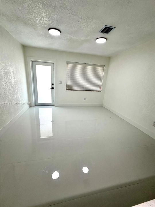 Polished large-format tile flooring, textured wall finish, dual flush-mount ceiling lighting, and a glass-paneled entry door