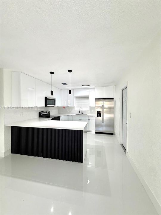 Kitchen featuring high-gloss white cabinetry, a center island with black vertical slat detailing, white stone-finish countertops, stainless steel appliances, and polished tile flooring