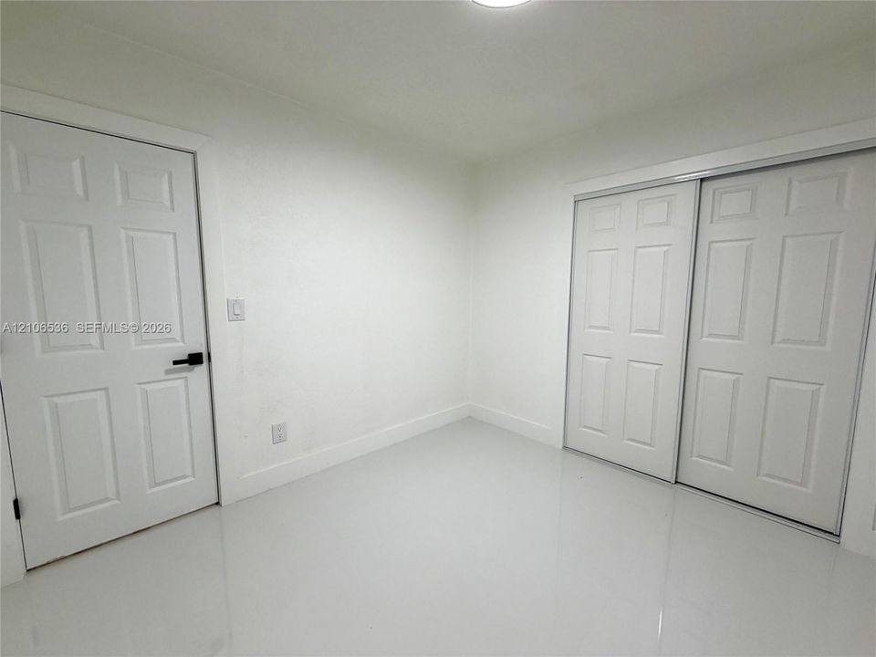 Neutral interior featuring smooth white walls, high-gloss floor tile, six-panel closet doors, and a six-panel entry door with matte black hardware
