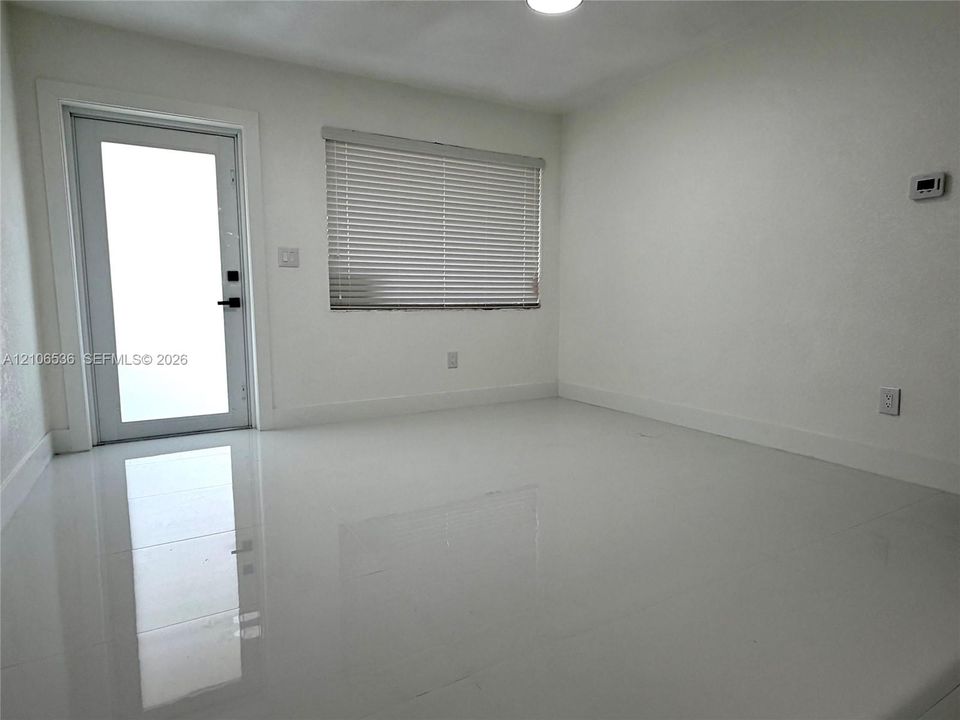 Interior space featuring polished white flooring, neutral wall finishes, a single-lite glass entry door, and a horizontal window with integrated blinds