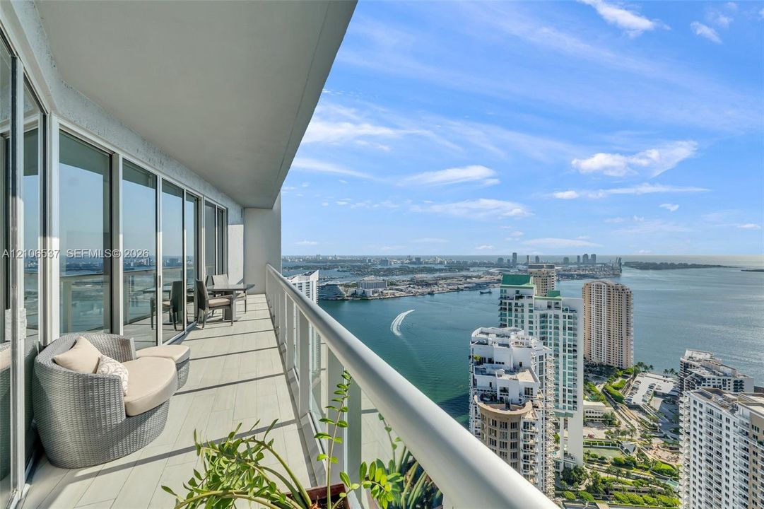 Covered terrace with porcelain tile flooring, full-height sliding glass doors, and a glass-paneled railing overlooking the waterway and cityscape