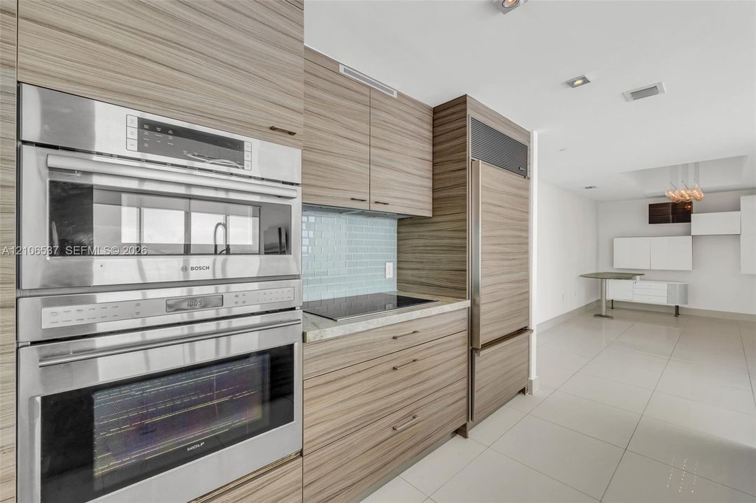 Kitchen featuring custom wood-grain cabinetry, integrated stainless steel refrigerator, Bosch wall oven and microwave, stone countertops, and tile backsplash