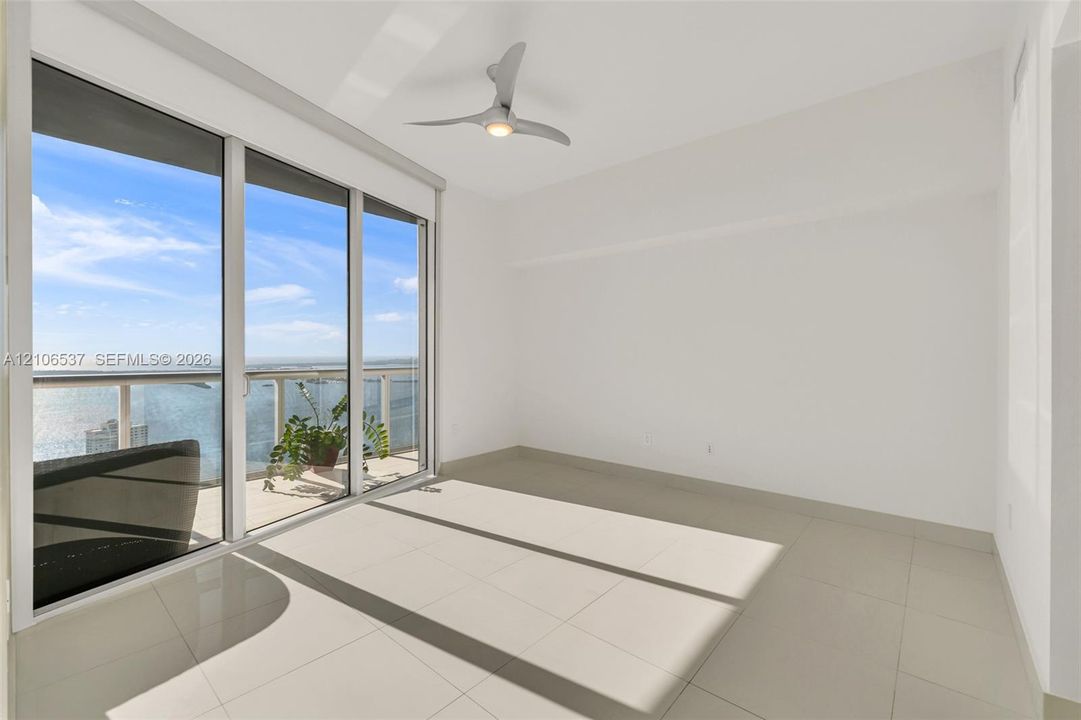 Floor-to-ceiling sliding glass doors, balcony with glass railing, large-format tile flooring, and contemporary three-blade ceiling fan