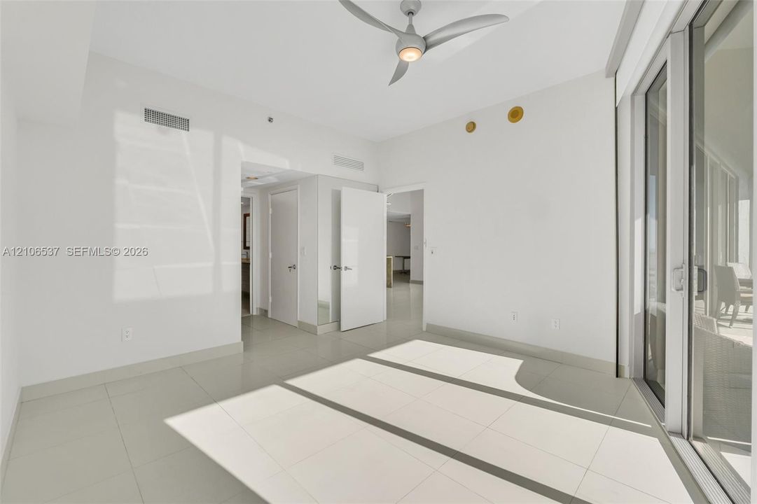 Neutral-toned interior featuring large-format tile flooring, a modern multi-blade ceiling fan, and expansive floor-to-ceiling glass sliding doors