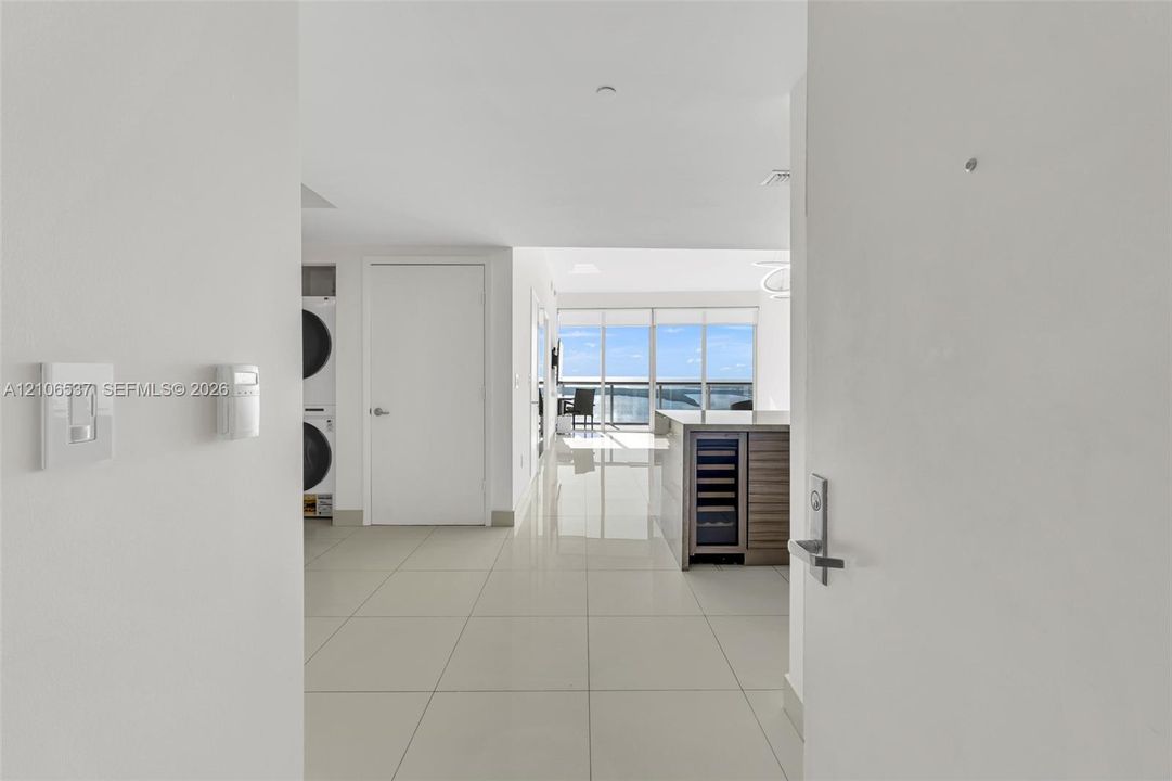 Large-format tile flooring, built-in wine refrigerator, wood-finish kitchen cabinetry, stacked laundry unit, and floor-to-ceiling windows